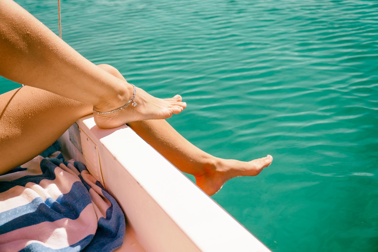 Bare feet over the side of a yacht above turquoise water