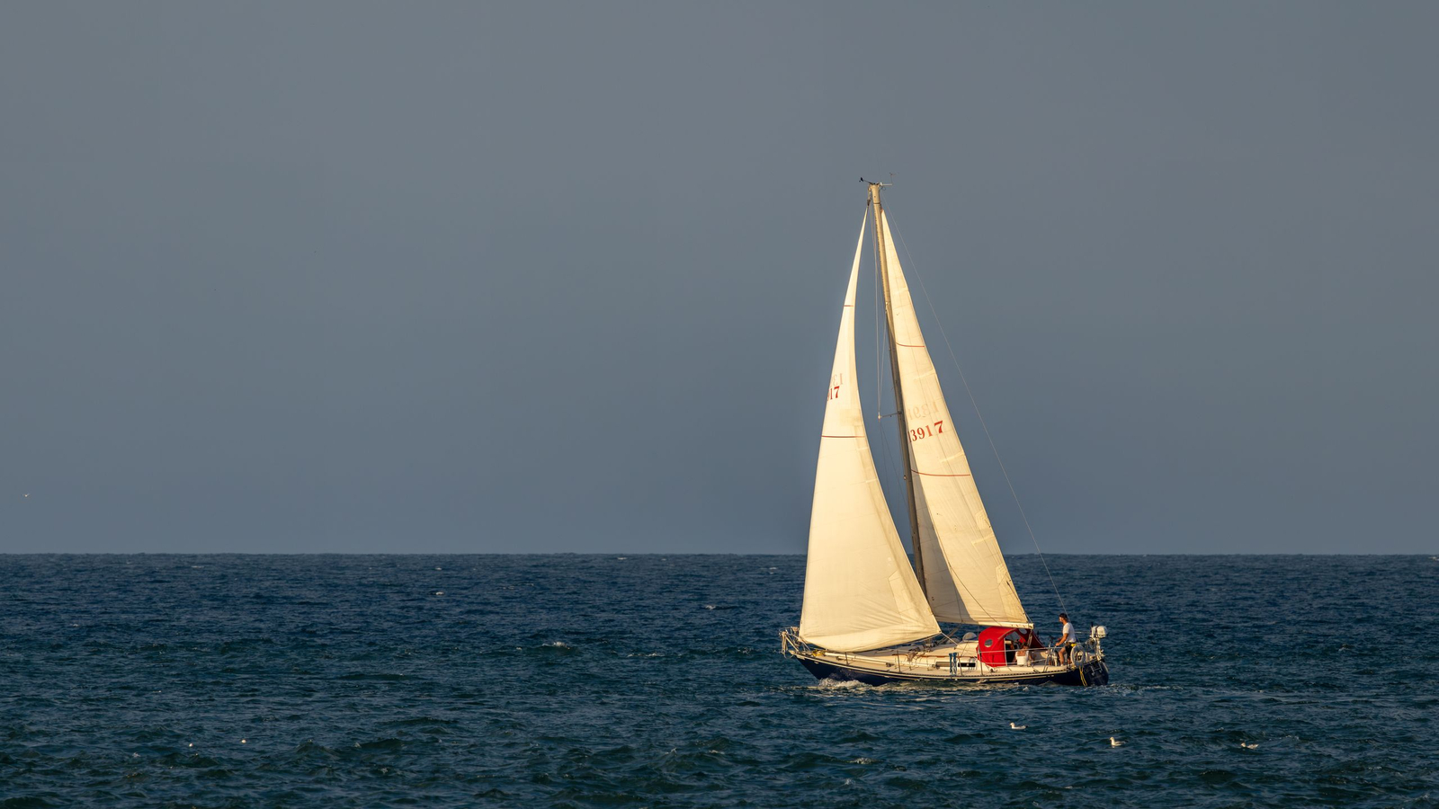 A sailboat gliding on the open sea under a sunset sky