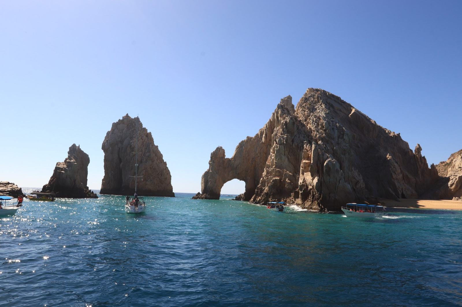 Boats crossing the bright blue water beside the Arch of Los Cabos