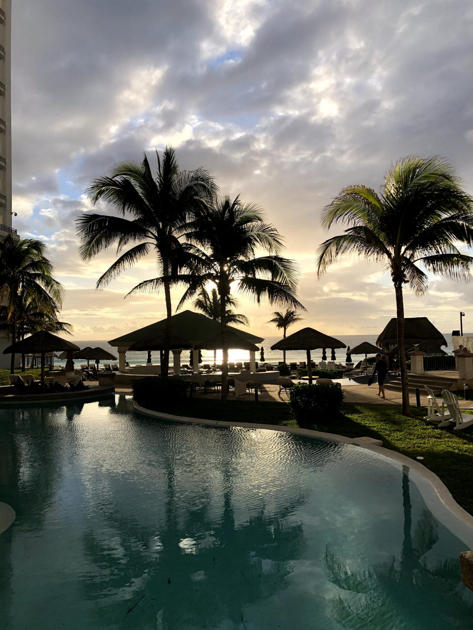 Beachside pool, cabanas and palm trees at sunset in Cancun